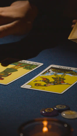 Vertical-Video-Close-Up-Of-Woman-Giving-Tarot-Card-Reading-On-Candlelit-Table